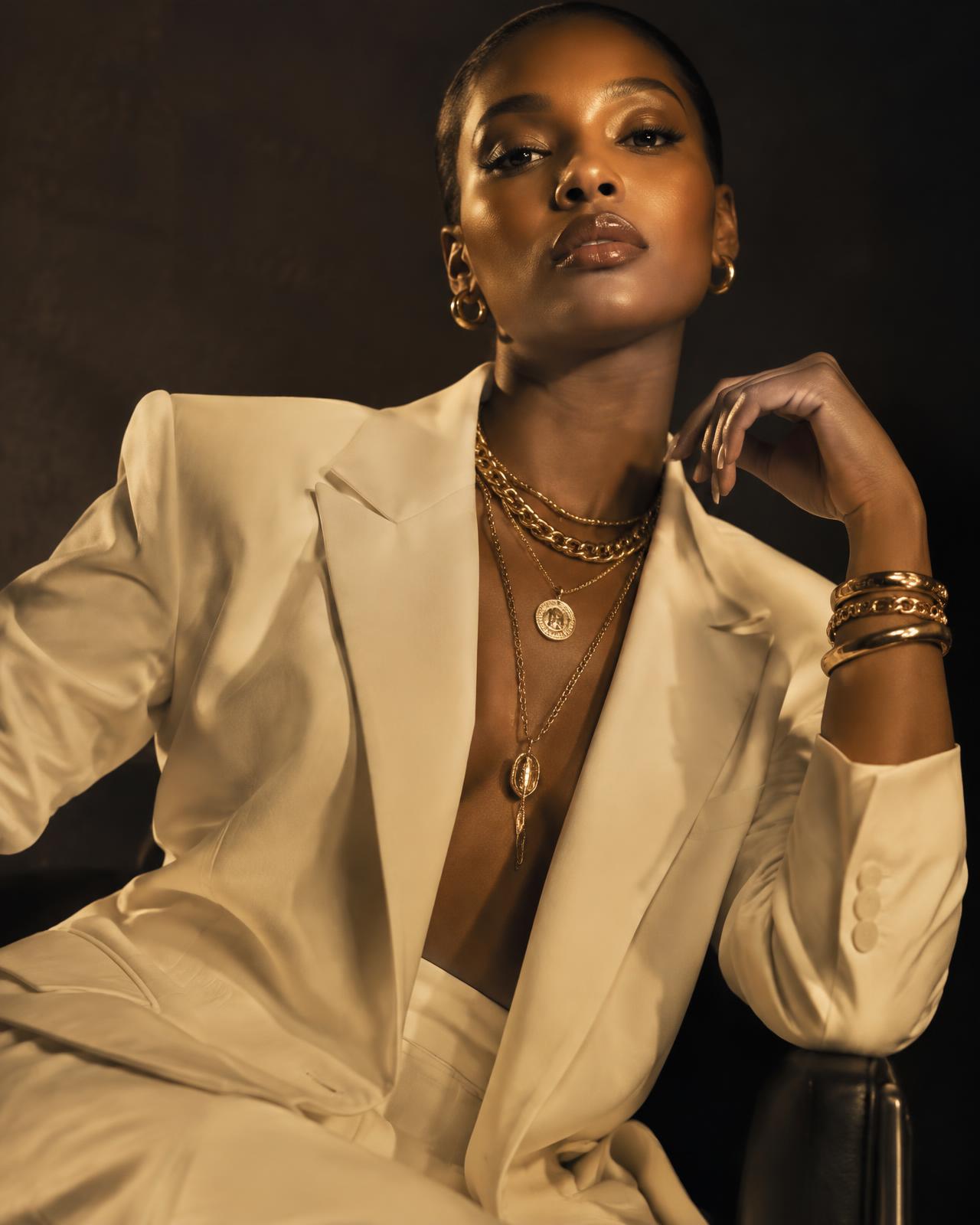 Model in cream blazer wearing layered gold chains and bracelets